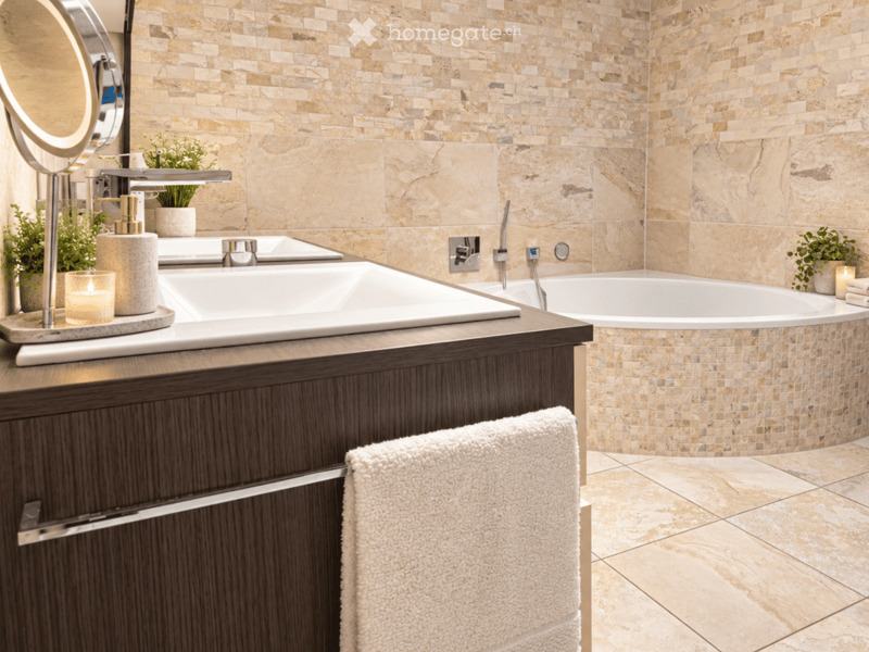 Modern bathroom with a large bathtub, a sink with a sleek faucet, a round mirror, a towel, a candle, a soap dispenser, and small decorative plants.