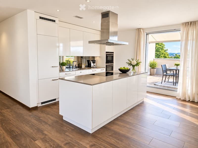 Modern kitchen with white cabinets, a central island, stainless steel appliances, and a view of a balcony with outdoor furniture.