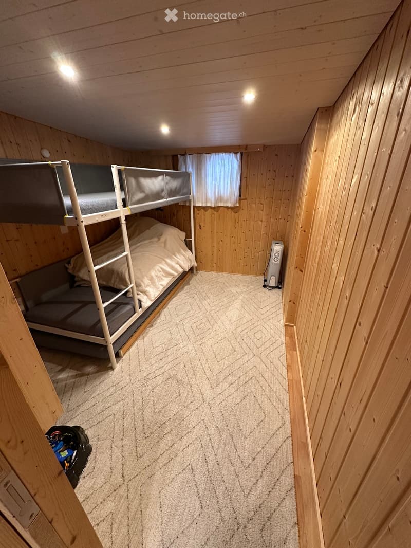Cozy wooden bedroom with a bunk bed, white bedding, and a small heater near the window.