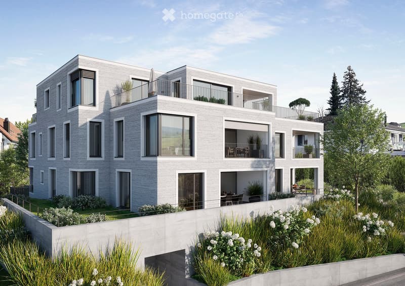 Modern two-story residential building with grey brick facade, large windows, balconies, and surrounding greenery.