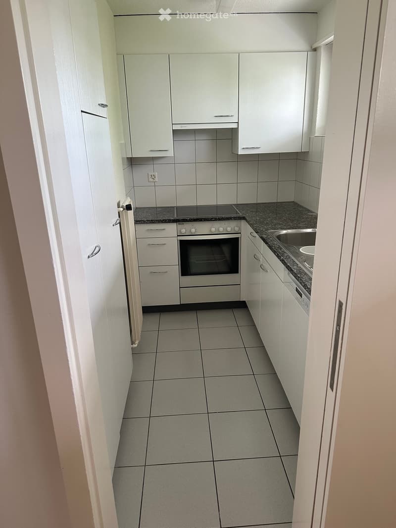 Modern kitchen with white cabinets, stainless steel oven, sink, and tiled countertops.