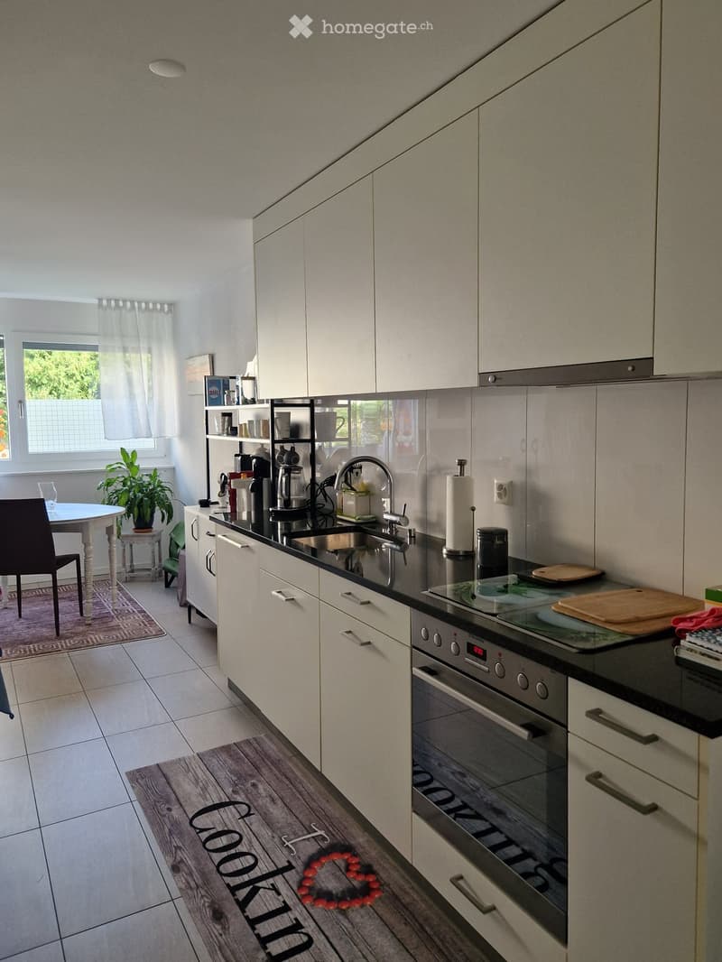 Modern kitchen with white cabinets, black countertops, stainless steel appliances, and a small dining area with a table and chair.