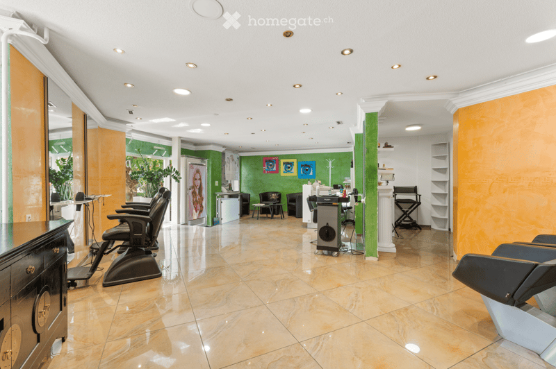 Modern salon with marble flooring, multiple black styling chairs, small round tables, mirrors, shelves, and decorative artwork.