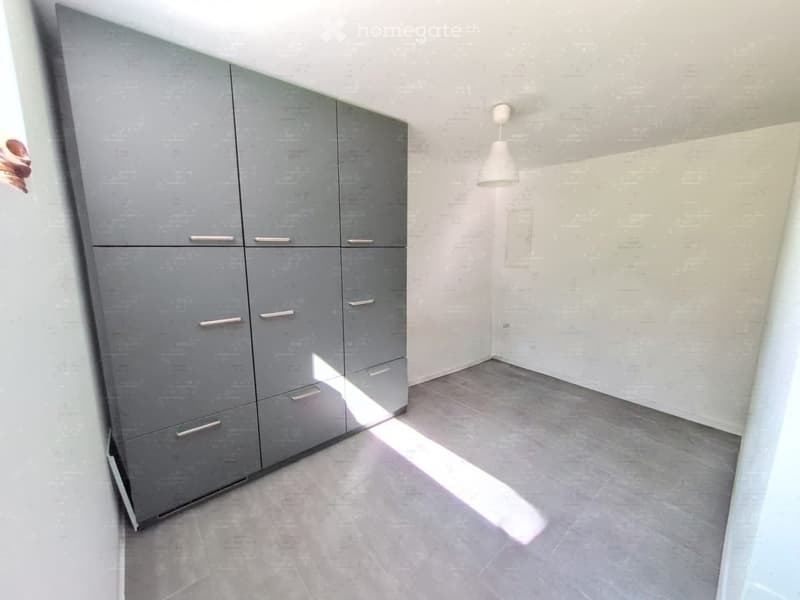 Empty room with grey cabinets, tiled floor, and a pendant light fixture.