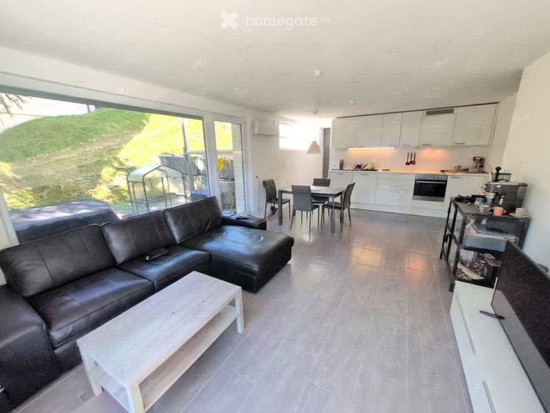 Modern living and dining area with a black leather sofa, white coffee table, dining table with chairs, and a fully equipped kitchen with white cabinets and stainless steel appliances.