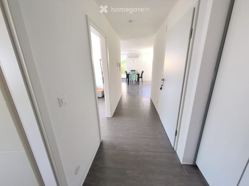 A clean, modern hallway with white walls, grey tiled floor, and several doors leading to different rooms.