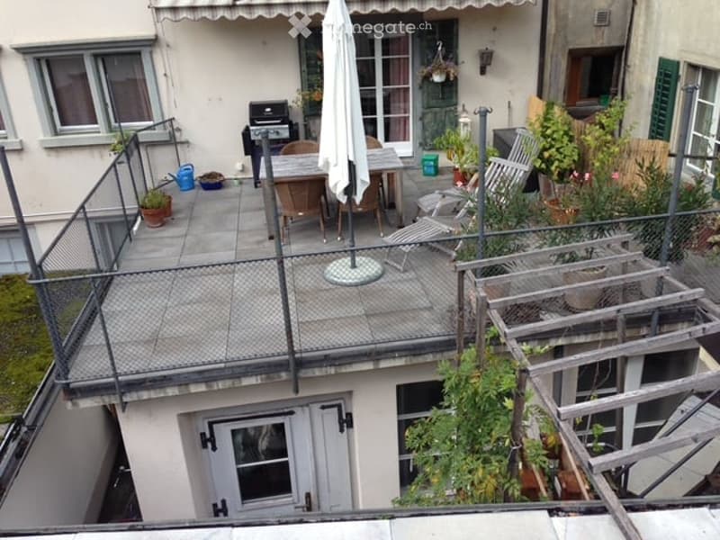 Balcony with a table, chairs, umbrella, grill, and potted plants.
