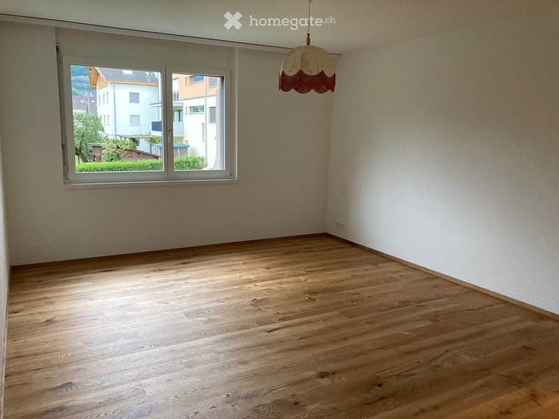 Empty room with wooden flooring, light-colored walls, and a large window offering a view of the outside area.