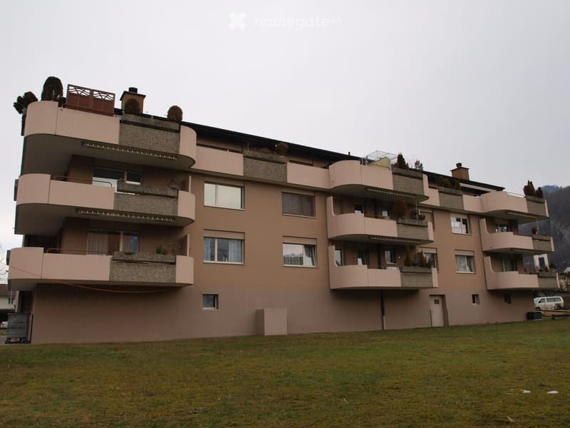 Modern multi-story residential building with multiple balconies and windows, surrounded by a grassy area.