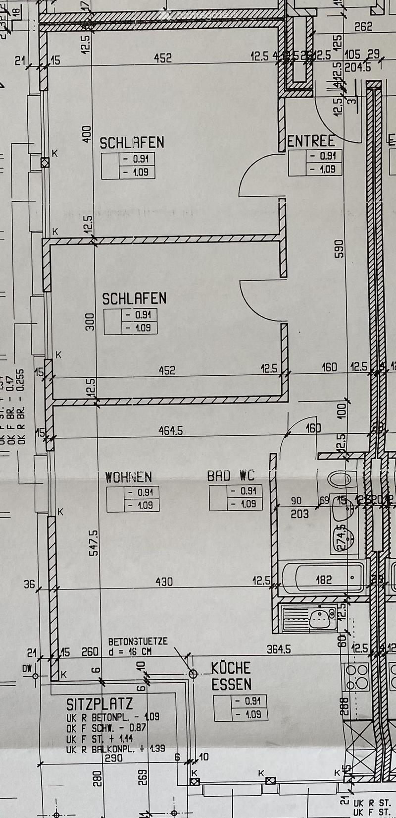 Floor plan showing a layout with labeled rooms: Schlafzimmer (bedroom), Wohnen (living room), Bad WC (bathroom), Küche Essen (kitchen and dining area), and Sitzplatz (seating area). Dimensions and measurements are indicated throughout.