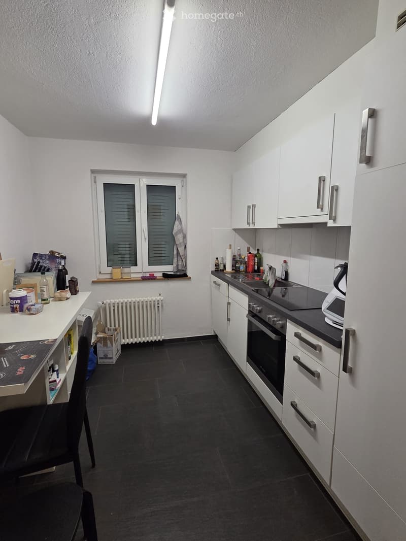 Modern kitchen with white cabinets, black countertops, and stainless steel appliances. Includes a sink, oven, and a small table with a chair.