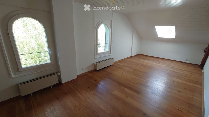 Empty room with wooden flooring, white walls, and large arched windows. Radiators are visible under the windows.