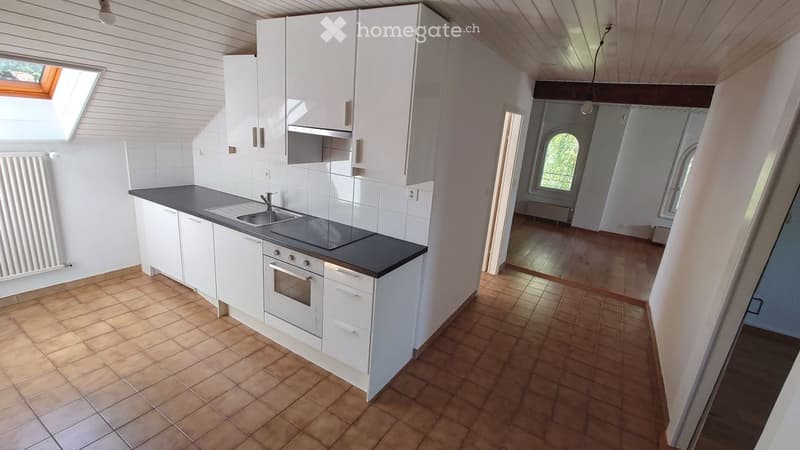 Modern kitchen with white cabinets, black countertop, stainless steel sink, and built-in oven. The space features tiled flooring and a skylight window.