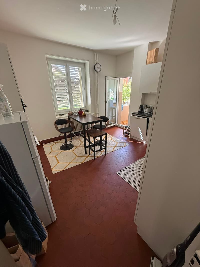 A modern kitchen and dining area with a hexagonal tile floor, a round dining table with chairs, and a small kitchen area with appliances.