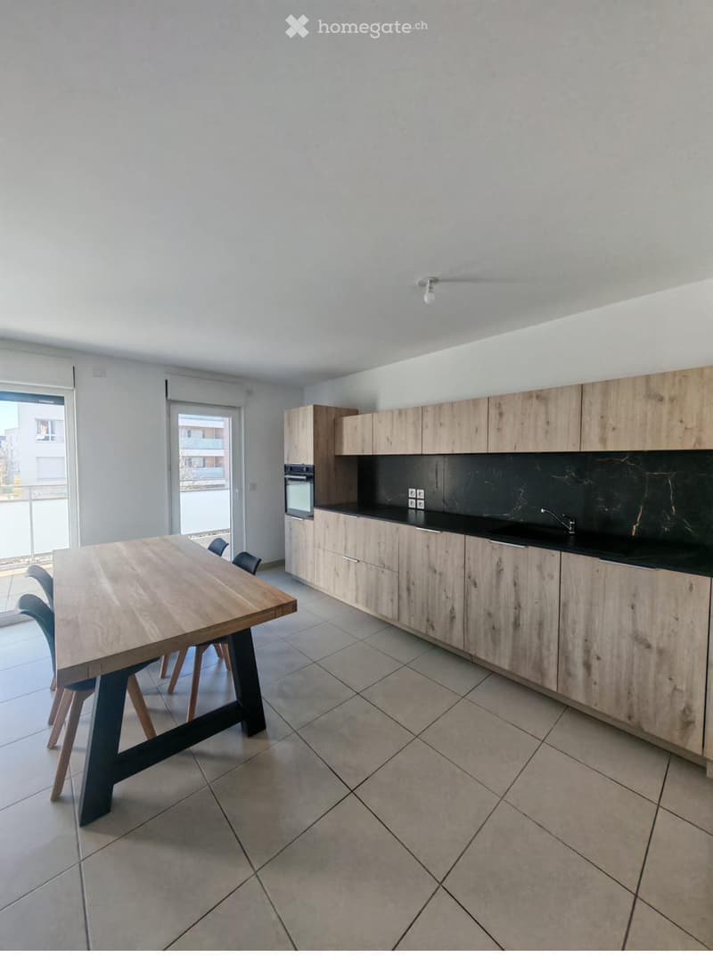 Modern kitchen with light wooden cabinets, black countertops, a wooden dining table with chairs, and an oven.