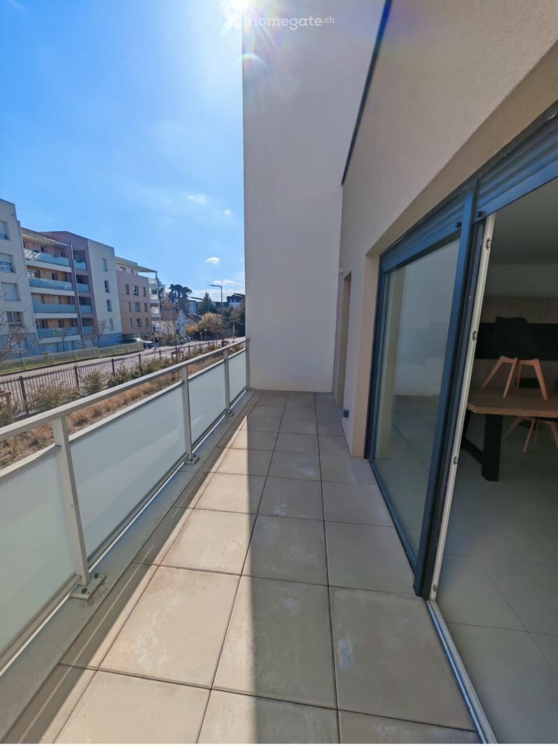 Balcony with tiled floor, glass railing, and view of the street and neighboring buildings.