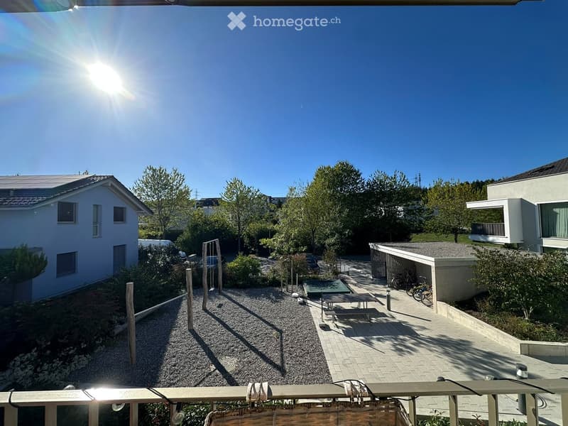 Balcony view of a residential area with houses, trees, bicycles, and outdoor furniture.