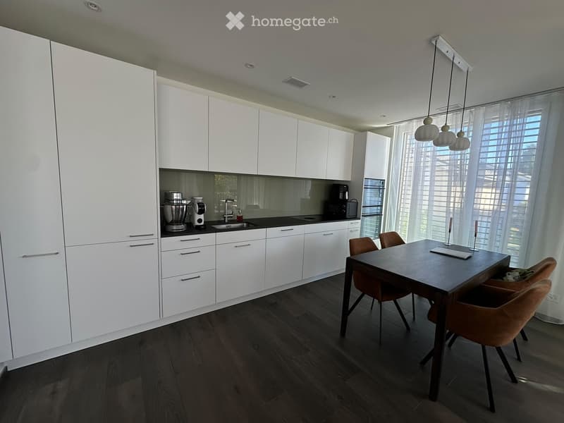 Modern kitchen with white cabinets, dark wooden flooring, a dining table with chairs, and various appliances including a blender, coffee maker, microwave, and oven.