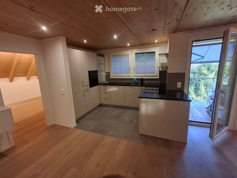 Modern kitchen with white cabinets, black countertops, and a wooden floor. Features an island with a sink and an oven, and large windows overlooking a balcony.