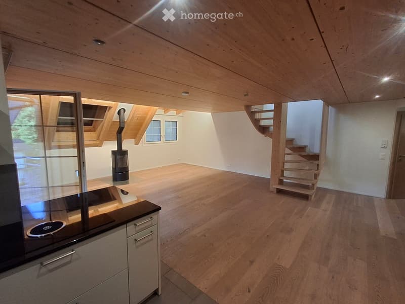 Bright, wooden-floored room with a modern kitchen area, a wood-burning stove, and a staircase leading to another level.