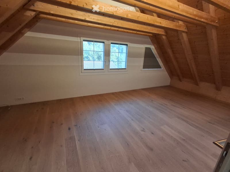 Empty attic space with wooden floors, exposed wooden beams, and three windows allowing natural light.