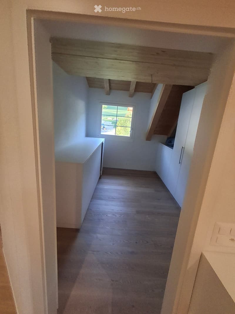Empty room with wooden floor, white walls, and a window showing a view of greenery outside. No furniture or equipment present.