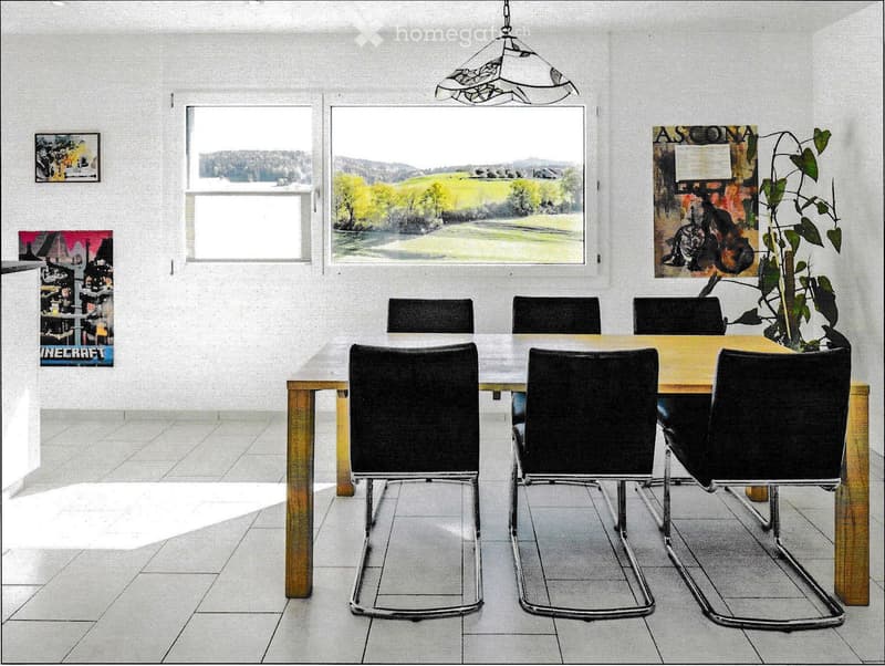 Dining room with a wooden table, six black chairs, pendant light, and a potted plant near the window. The room has large windows showing a scenic view.