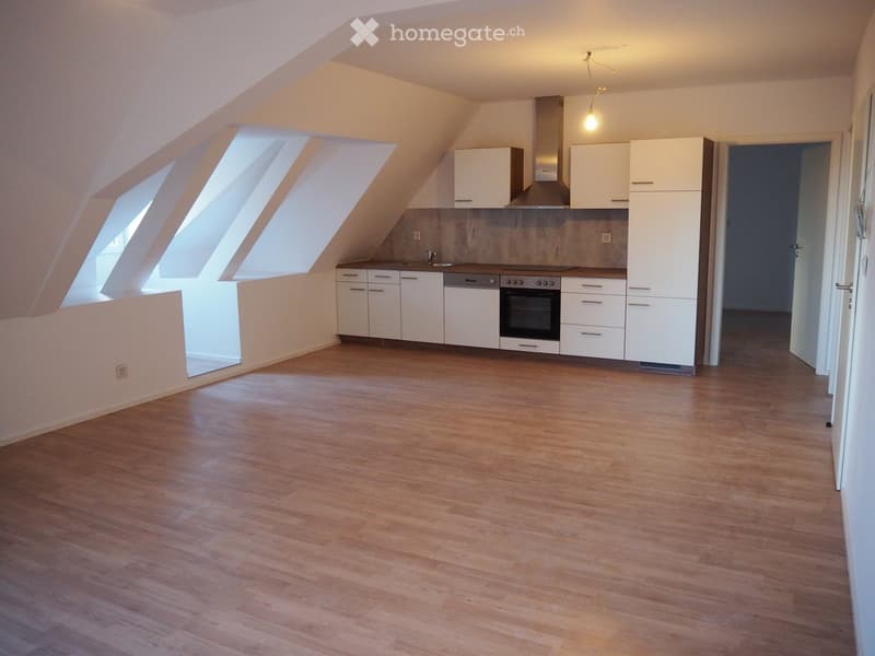 Empty attic room with wooden flooring, white kitchen cabinets, and large skylight windows.