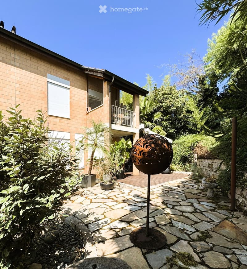 Garden area with stone pathway, decorative metal sphere, potted plants, and a small balcony overlooking the space.