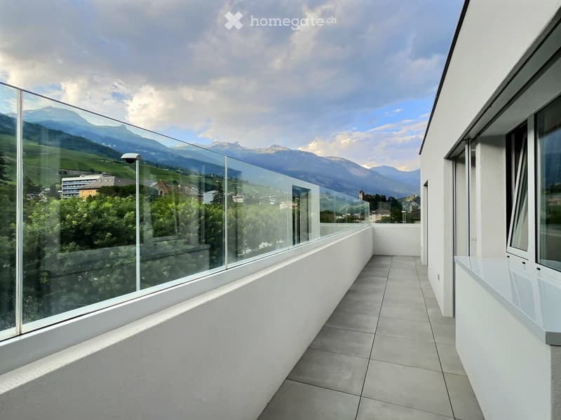 Modern balcony with large glass railings, tiled floor, and scenic mountain view.