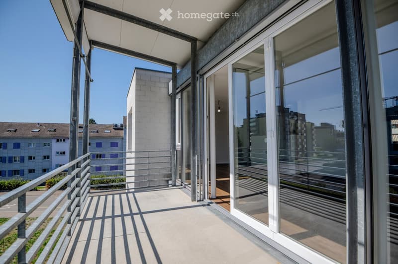 Modern balcony with glass sliding doors, metal railing, and a view of the surrounding urban area and buildings.