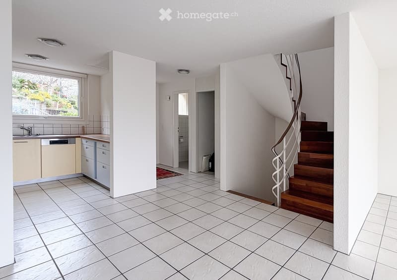 Bright, modern kitchen with white tiled flooring, light-colored cabinets, a sink, and a dishwasher. A wooden staircase with a metal handrail leads to an upper level.