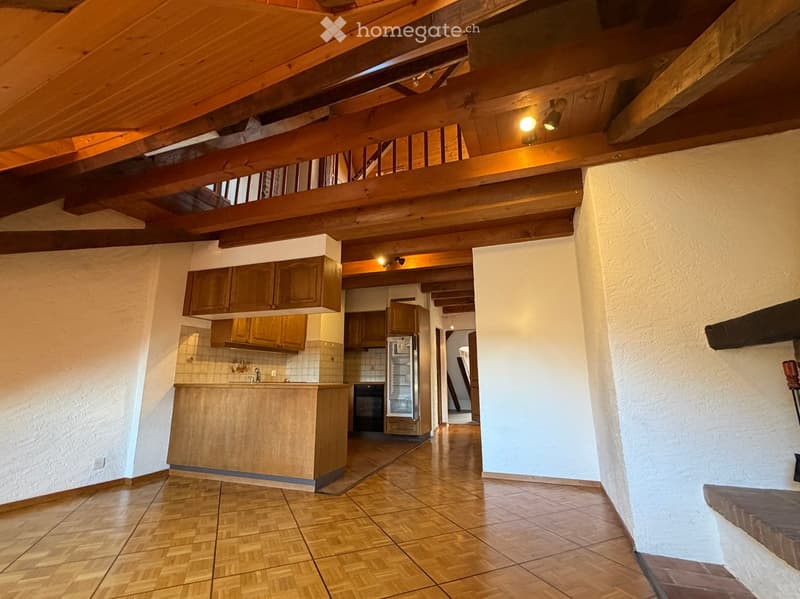 Open-plan living and kitchen area with wooden beams, tiled floor, and wooden kitchen cabinets.