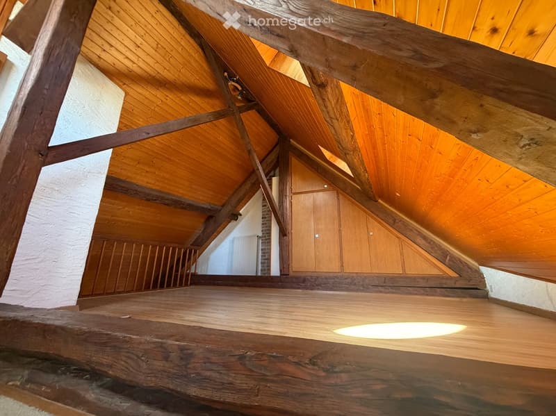 Attic hallway with exposed wooden beams and ceiling, wooden floor, built-in wooden cabinets, and a recessed light fixture.
