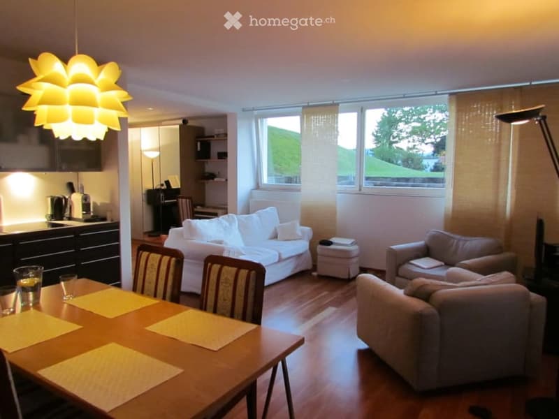 dining table with chairs, 2 couches, white sofa with cushions, white ottoman, floor lamp, large windows, kitchen in background