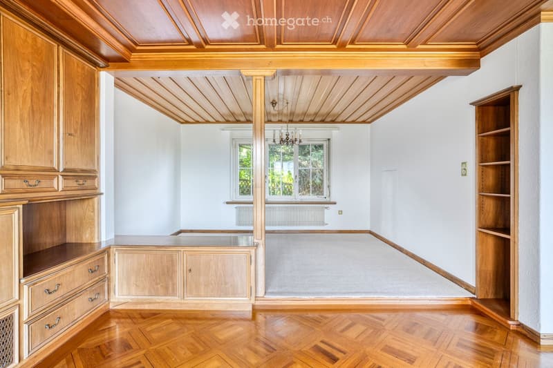 An empty room with wooden walls, a wooden ceiling, and a wooden floor. The room features built-in wooden cabinets and shelves, with large windows allowing natural light to enter.