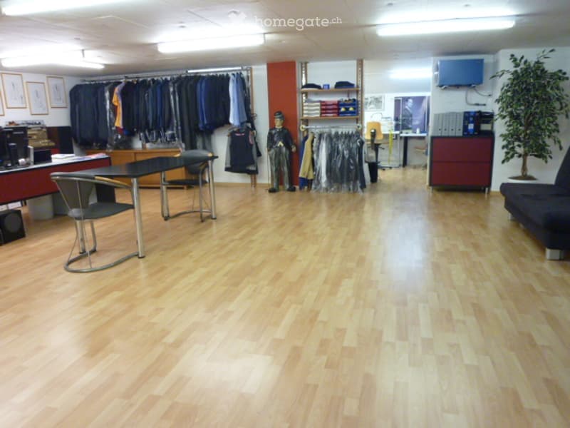 A well-lit room with wooden flooring, a clothing rack with various garments, a mannequin in uniform, a sofa, a table with chairs, a television, and framed pictures on the wall.