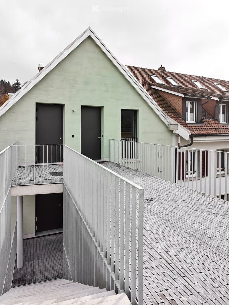 Two-story house, green and brown roof, two black doors, white railings, brick flooring