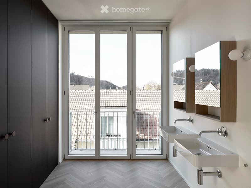 Modern bathroom with two white sinks, a large mirror cabinet, and a sliding glass door offering a view of rooftops and greenery.