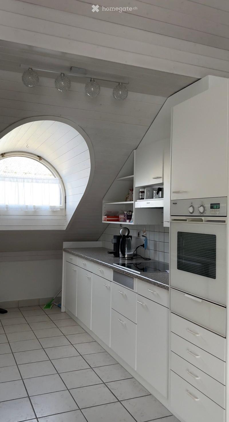 Modern kitchen with white cabinets, granite countertop, built-in oven, coffee maker, and shelves. Features a skylight window and pendant lights.