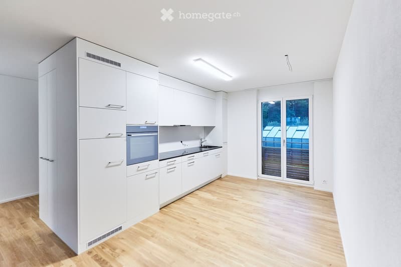 Modern, minimalist kitchen with white cabinets, a built-in oven, a sink, and a large window offering a view of the outdoor area.