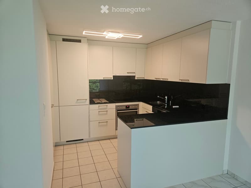 Modern kitchen with white cabinets, black countertops, and stainless steel appliances including an oven and sink.
