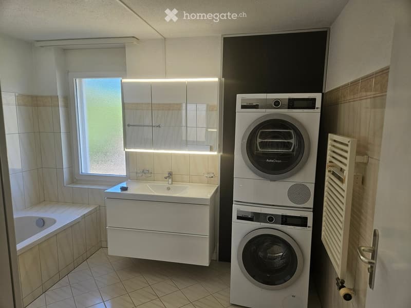 Modern bathroom with a white sink, bathtub, mirror cabinet, and stacked Bosch washing machine and dryer.