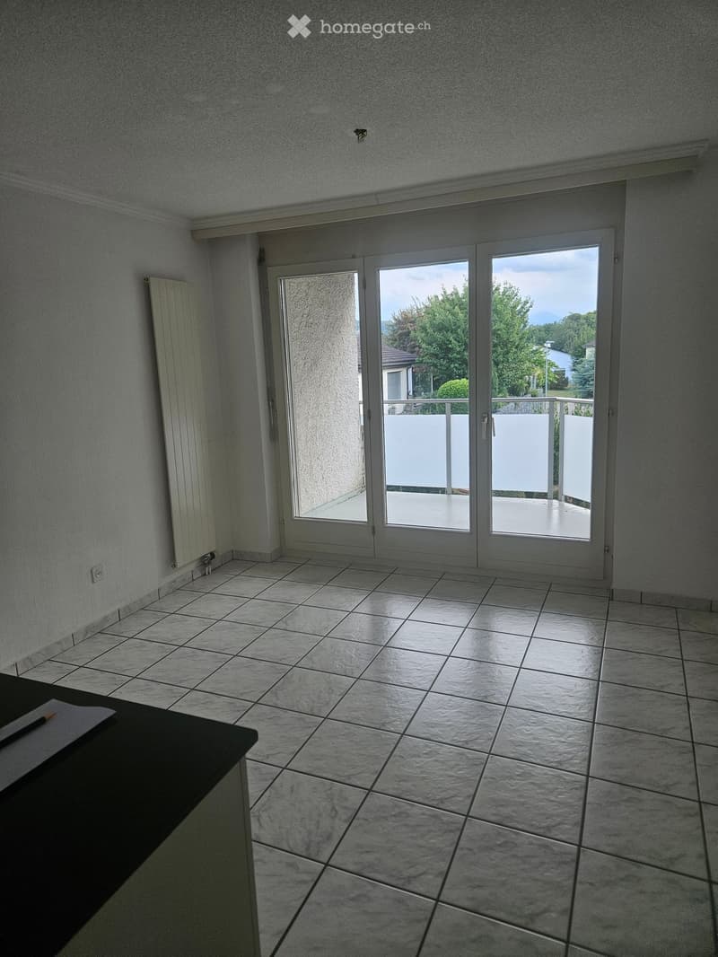 Empty room with tiled floor, white walls, and large sliding glass doors leading to a balcony with a view of greenery.