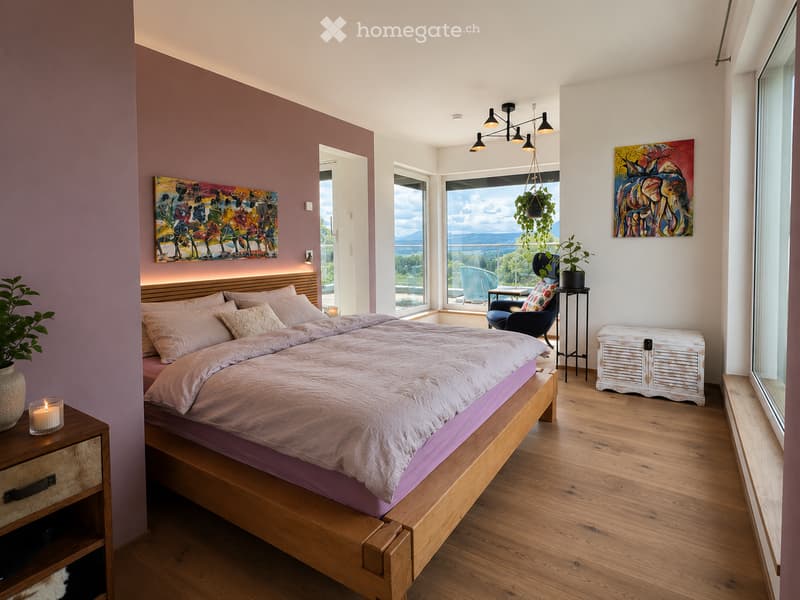 Modern bedroom with a wooden bed, nightstand, chair, and large windows offering a scenic view. Features include a chandelier, potted plants, and artwork on the walls.