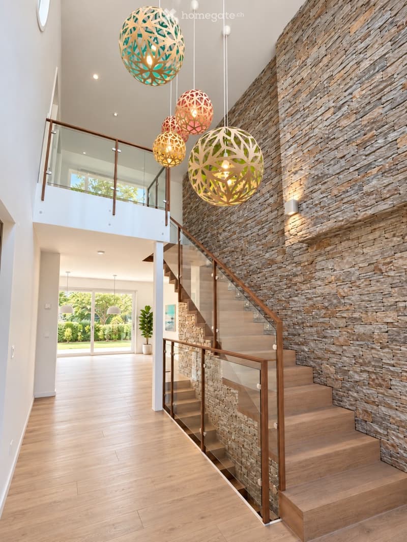 Modern hallway with wooden flooring, a staircase with glass railing, stone wall, and decorative pendant lights.
