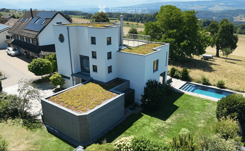Modern two-story house with white exterior, green roof, large windows, and a swimming pool in the garden.