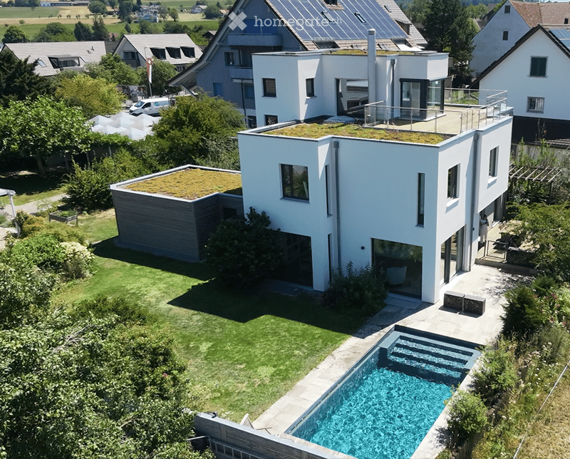 Modern white house with a green roof, surrounded by a well-maintained garden and a swimming pool.
