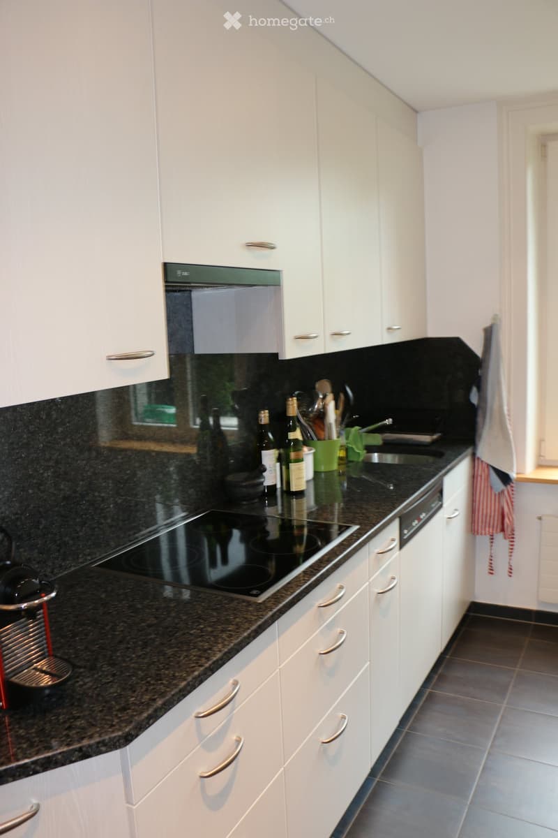 Modern kitchen with white cabinets, granite countertops, induction stove, coffee maker, and various kitchen items on the counter.