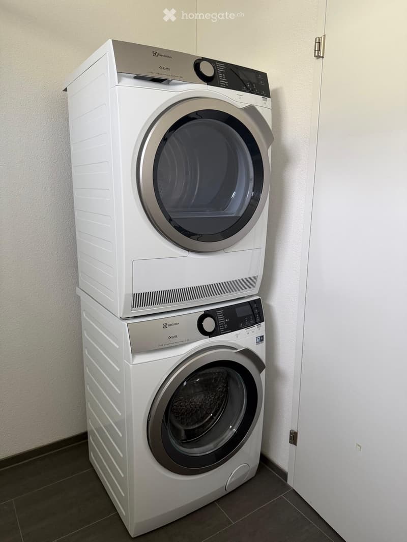 A modern bathroom features a stacked washing machine and dryer unit with sleek white finishes and digital control panels.